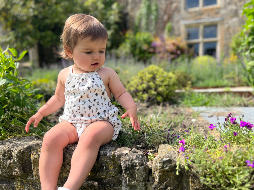 toddler sat on old stone wall wearing white bubble with shoe string straps in seahorse print