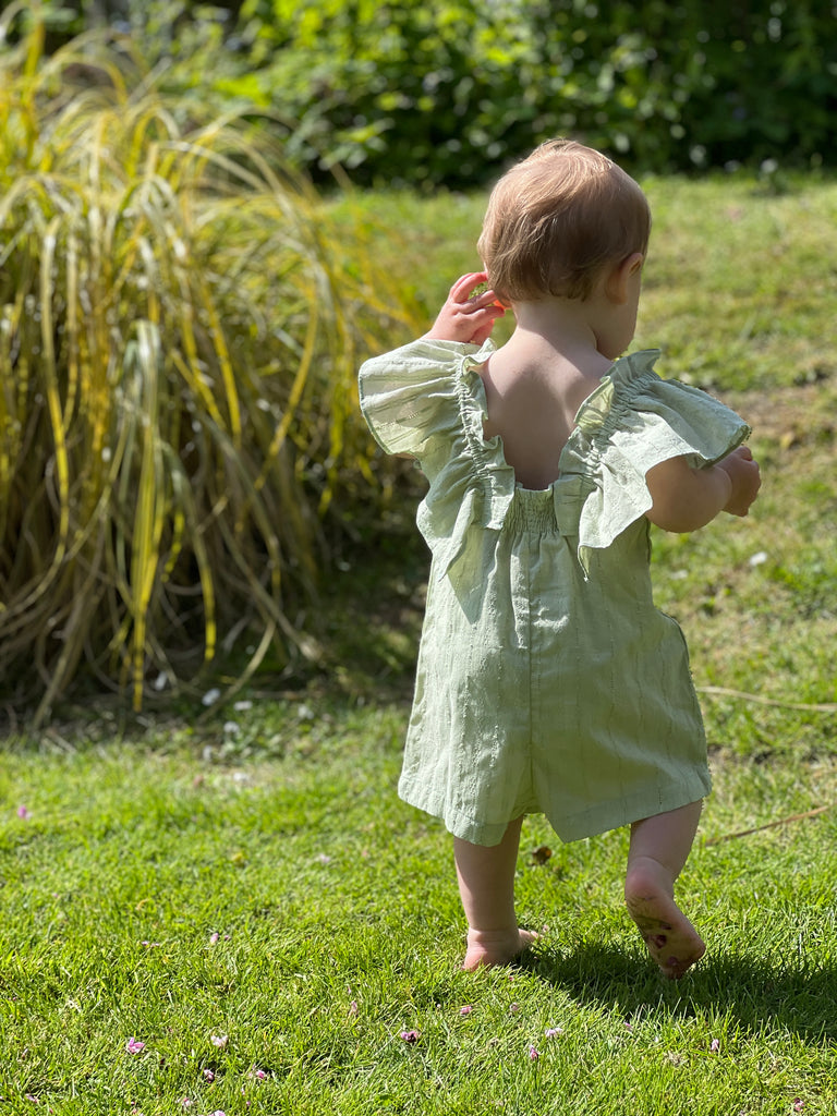 toddler in sunshine on lawn wearing pretty green all in one romper in pointelle fabric big frill sleeves
