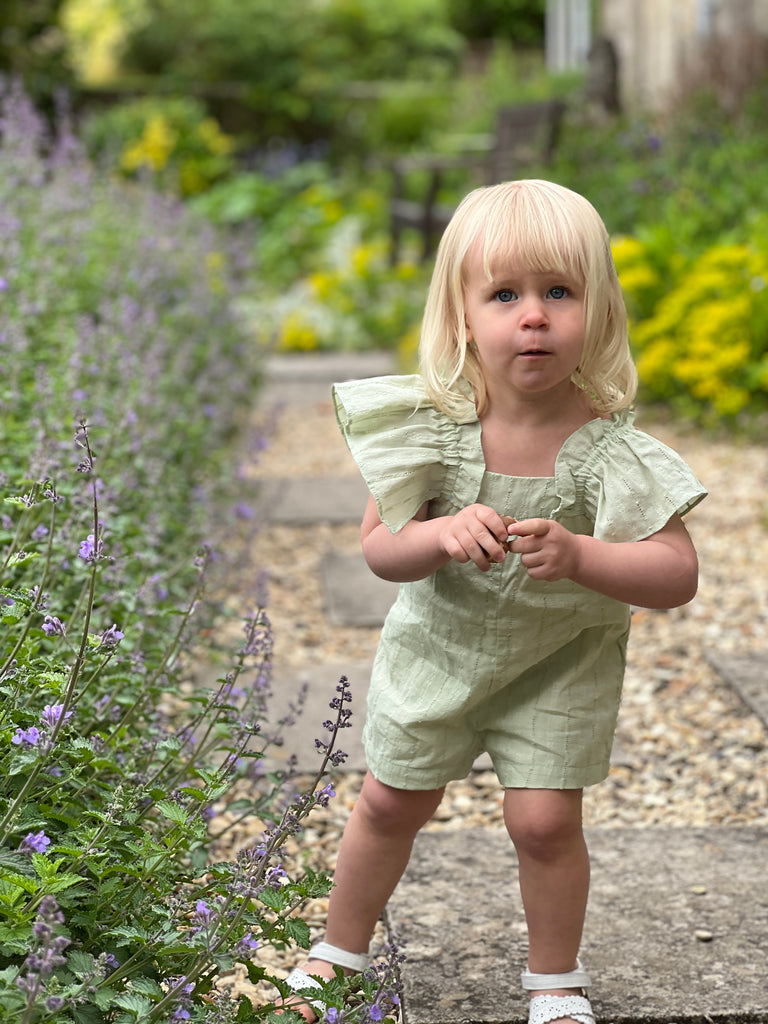 toddler in sunshine on path wearing pretty green all in one romper in pointelle fabric big frill sleeves