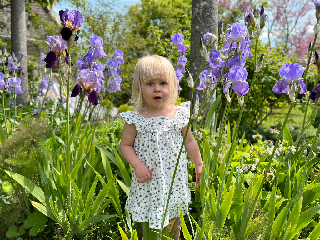 girl standing in summer garden flowers on sunny day wearing white dress with flower print frill shoulders hem frill