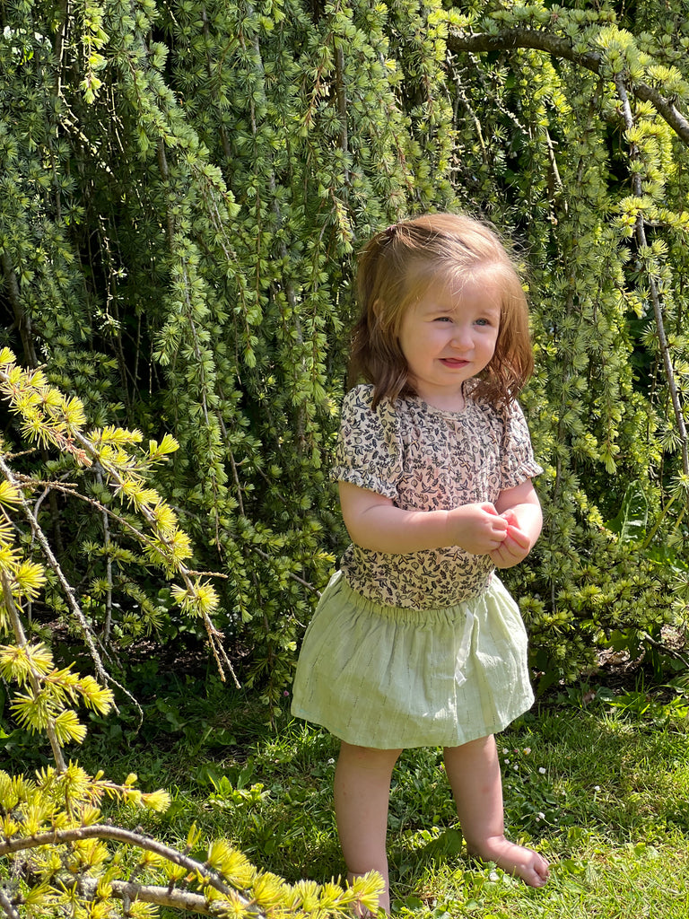 happy toddler in sunny garden wearing delicate green skort and flower cream top