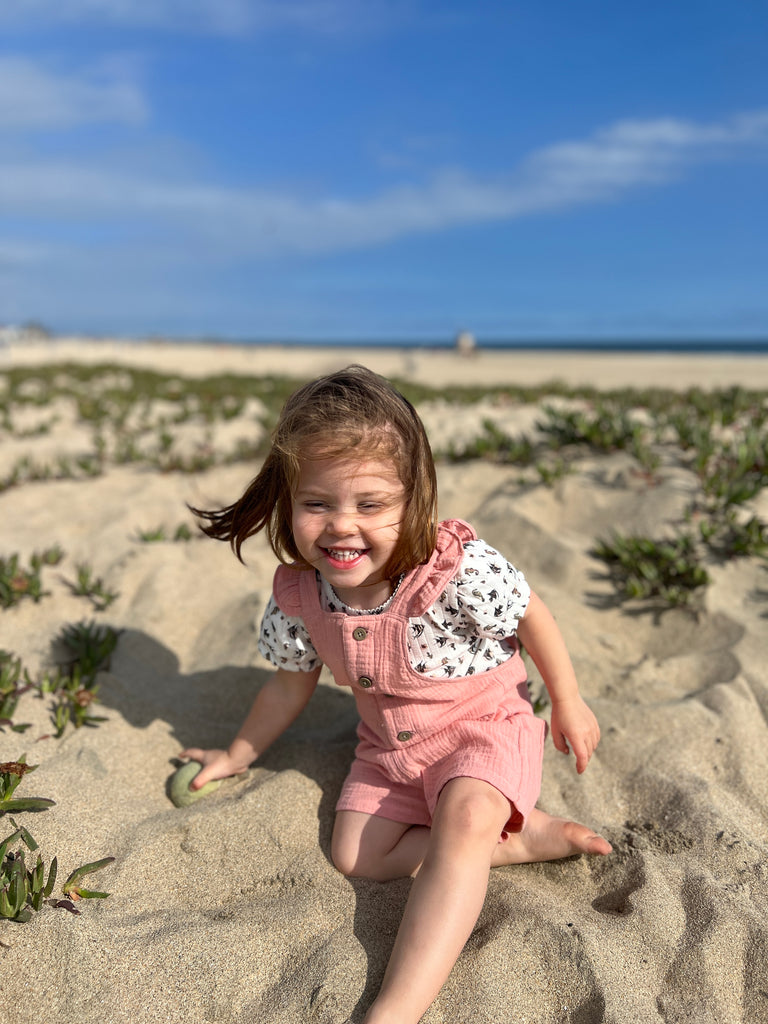 happy laughing girl on beach in the sunshine wearing tee shirt in white ribbed jersey with seahorse print under pink overalls