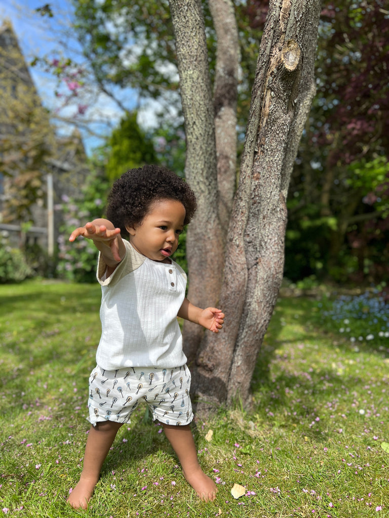 toddler standing in front of tree on sunny day wearing white jersey shorts with drawstring waist all over guitar tree print and white tee shirt
