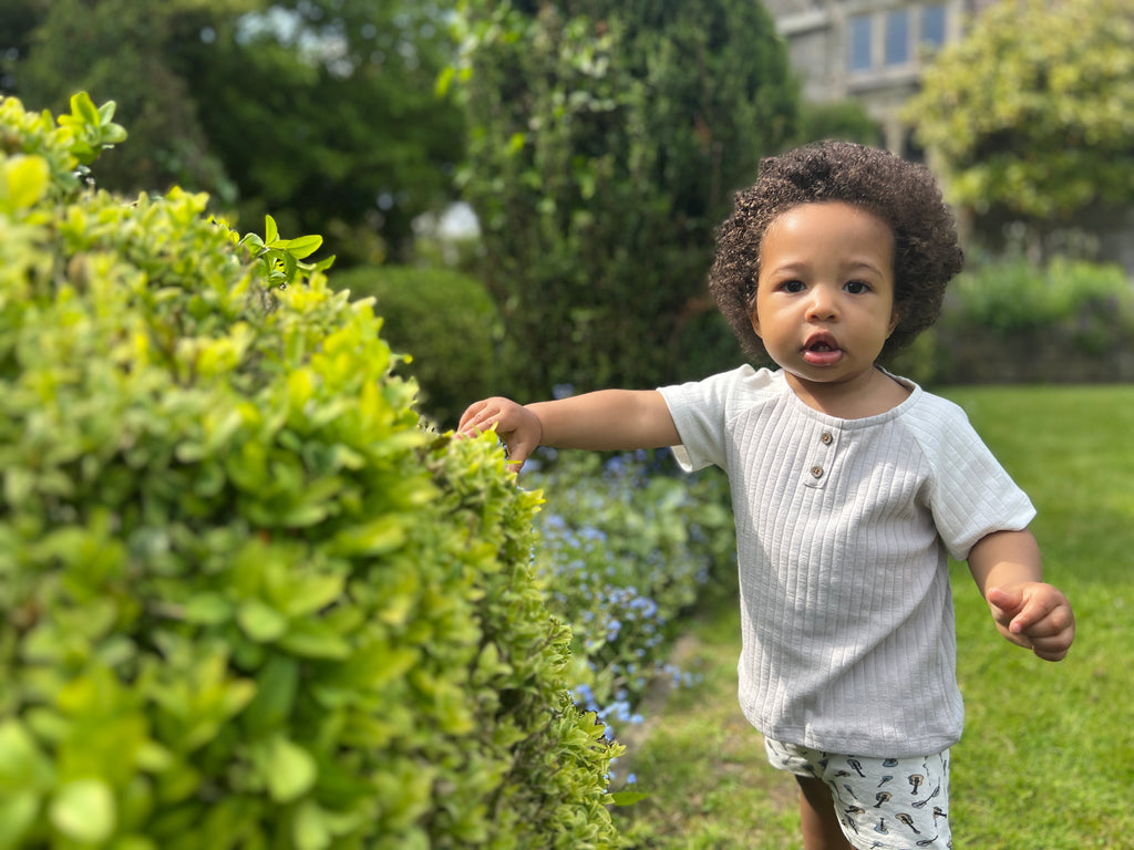 toddler standing in front of green bushes on sunny day wearing white jersey shorts with drawstring waist all over guitar tree print and white tee shirt
