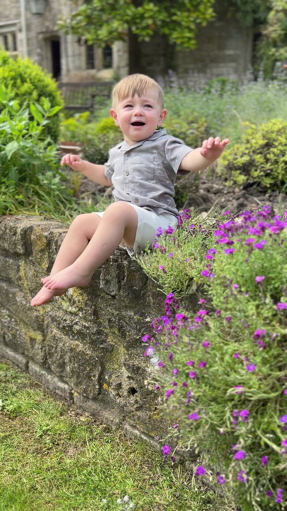 boy in sunny garden wearing white gauze shorts with side patch pockets and elasticated waist and grey shirt