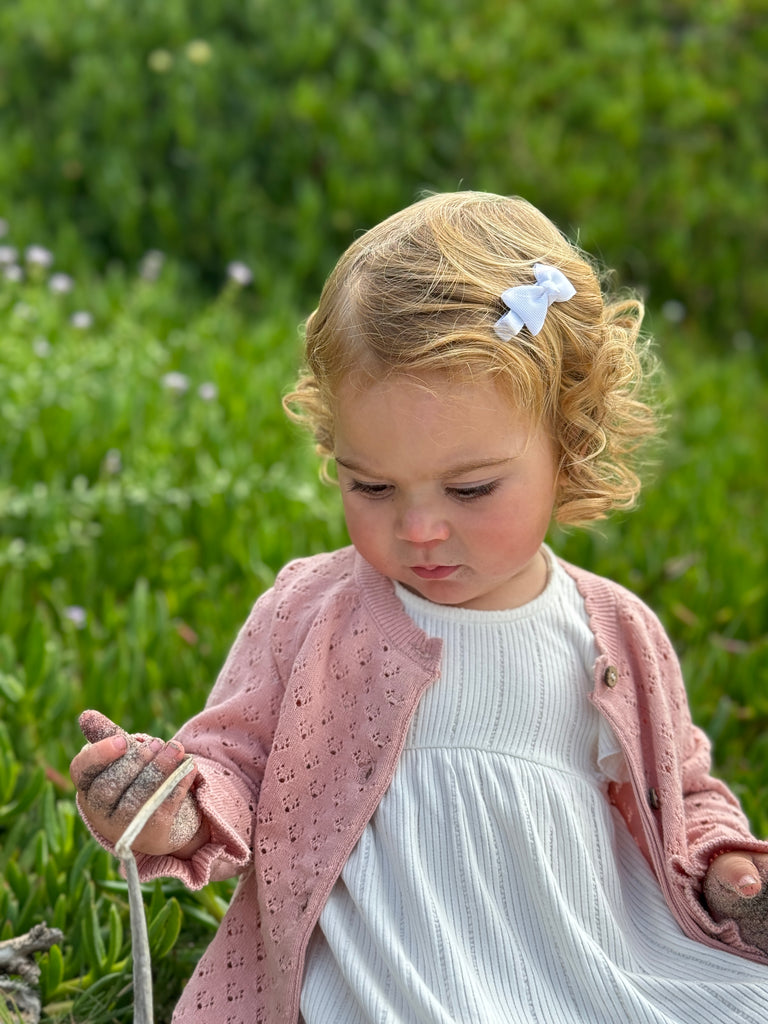 toddler sat in summer flower field wearing white dress and pink knit cardigan with pretty pattern, scalloped edge around the neck and the bottom and cute frill cuffs with a gentle stretch wrist band. Buttons down the front.