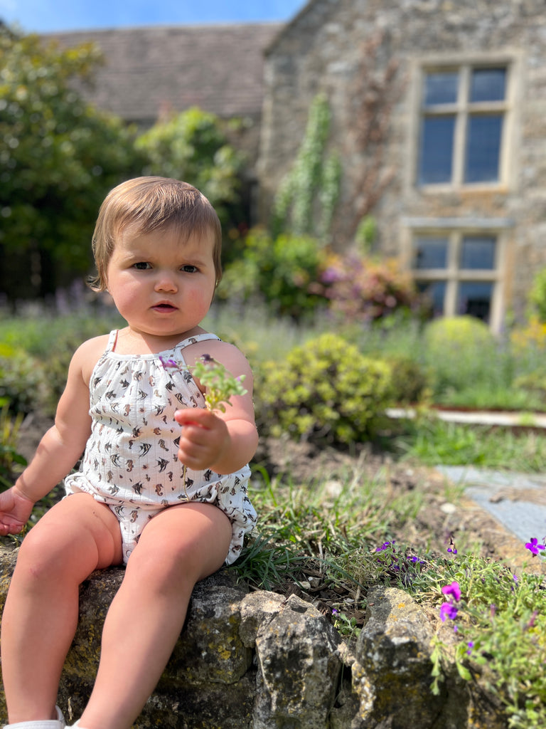 toddler sat on old stone wall wearing white bubble with shoe string straps in seahorse print 