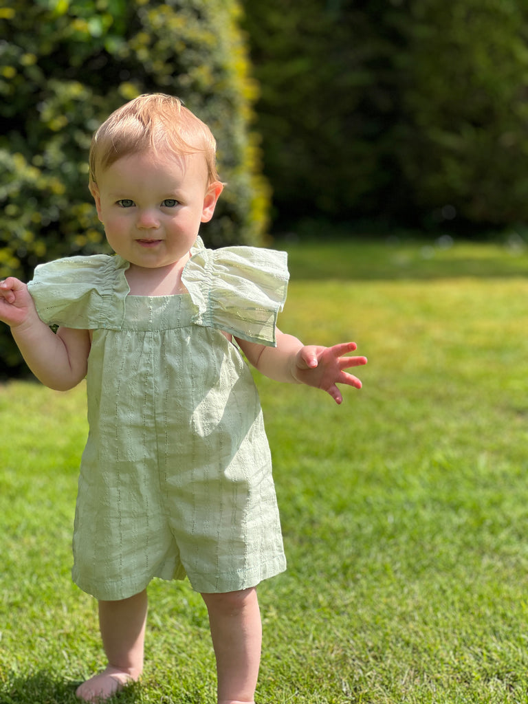 toddler in sunshine on lawn wearing pretty green all in one romper in pointelle fabric big frill sleeves