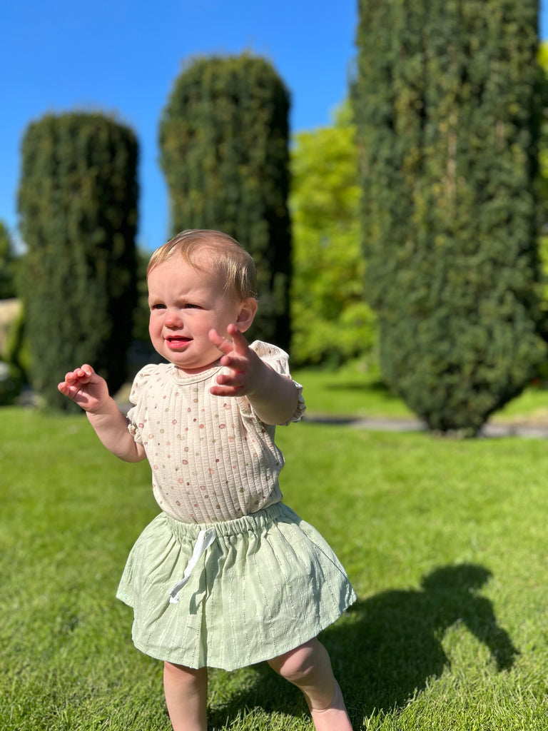 happy toddler in sunny garden wearing delicate green skort and spotty cream top