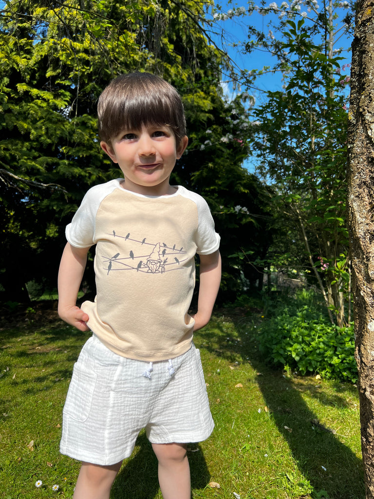 boy in sunny garden wearing white gauze shorts with side patch pockets and elasticated waist and print tee