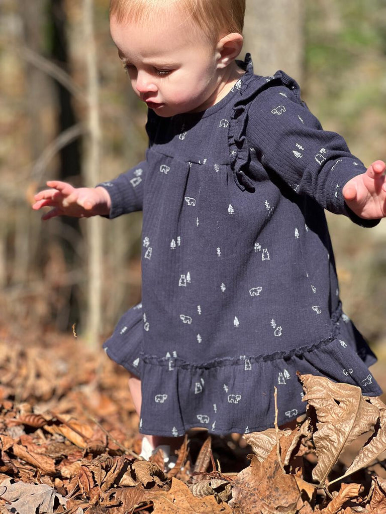 toddler playing in autumnal wood wearing navy blue dress with bear print with ruffle shoulders and long sleeves ruffle frill around the bottom