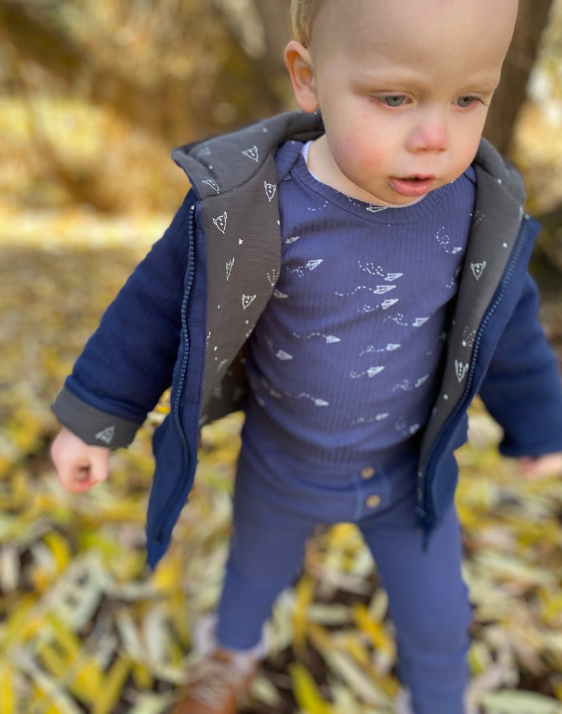 toddler standing in autumnal wood wearing padded jacket zip front with hood navy jersey with rocket print lining
