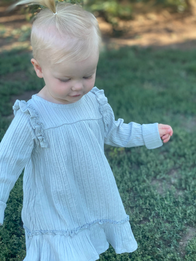 toddler wearing pale grey dress with ruffle shoulders and long sleeves ruffle frill around the bottom