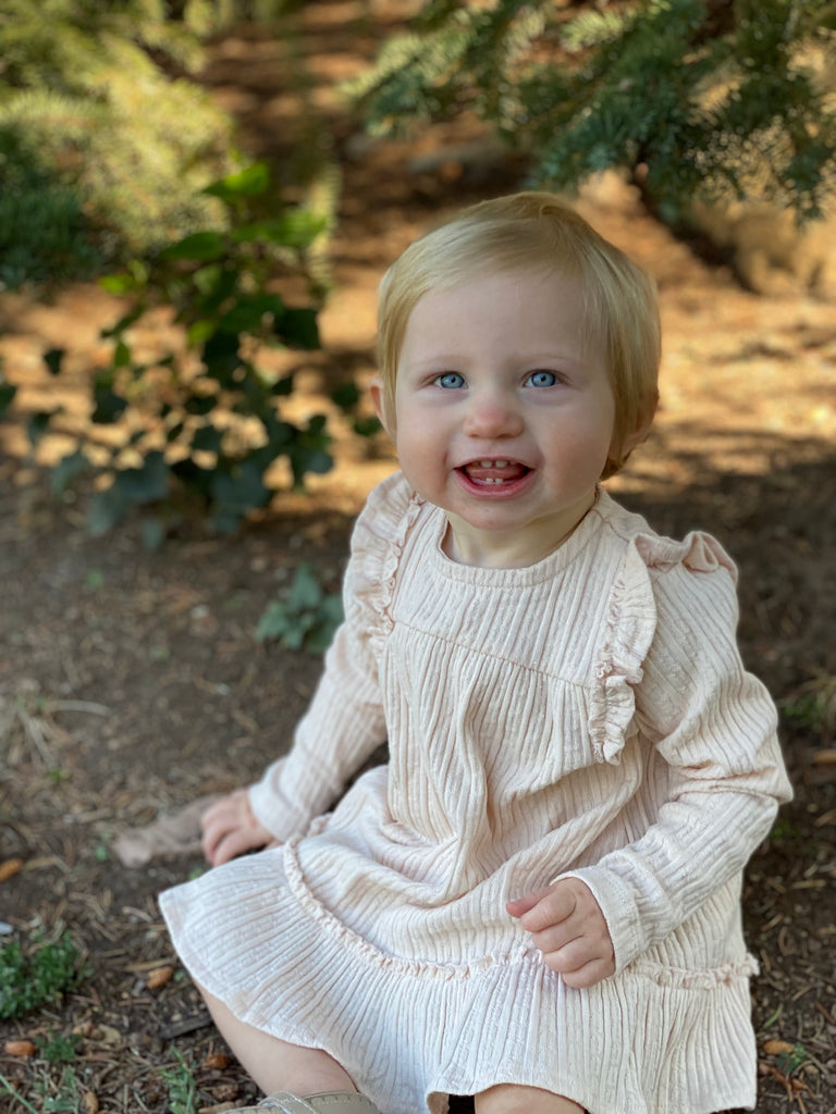 happy toddler in autumn wood wearing cream dress with ruffle shoulders and long sleeves ruffle frill around the bottom
